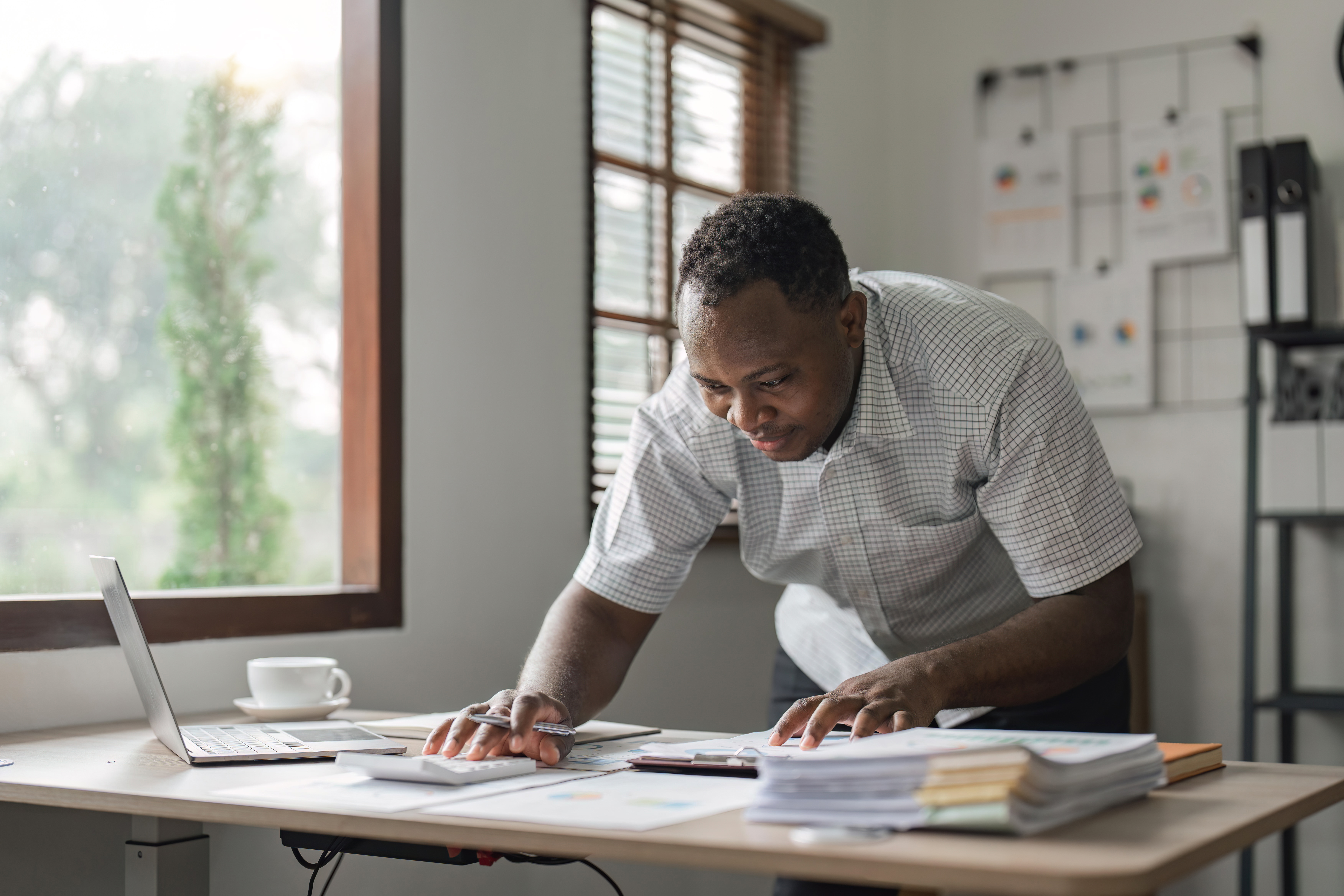 Happy African man using laptop computer and calculator for calculating invoice at home