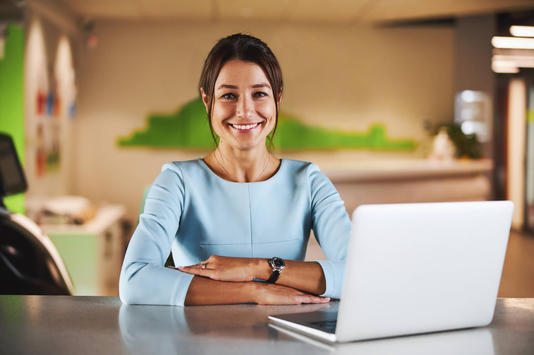 Happy attractive brunette virtual assistant working at the laptop in conference room